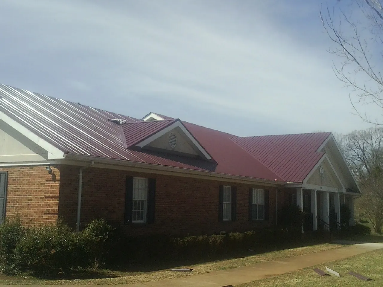 Red metal roof with gabled entries on a long brick building, from a Hail Damage Roof Repair job in Bainbridge