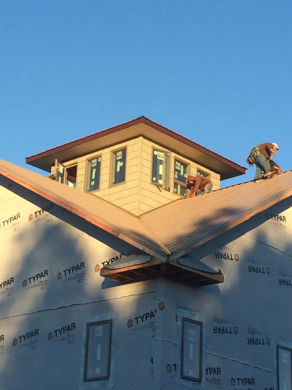 Roofers working around a rooftop cupola on a new metal roof at sunset in Bainbridge